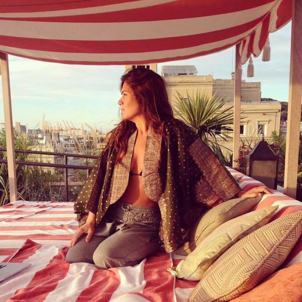 Woman sitting on a sunny rooftop with a striped canopy and cityscape view wearing a polkadot jacket from Violet Elizabeth